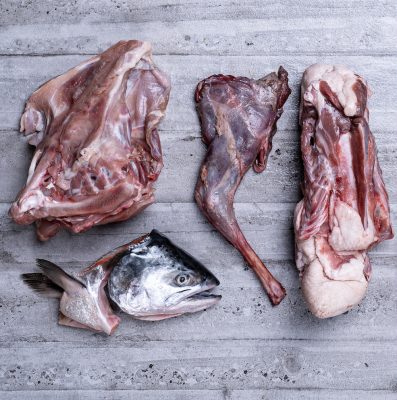 Assortment of cuts of meat on a slate board including chicken frame, duck frame, wallaby shoulder, fish head
